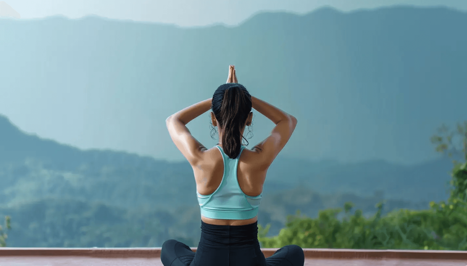 Woman in seated prayer pose overlooking mountains